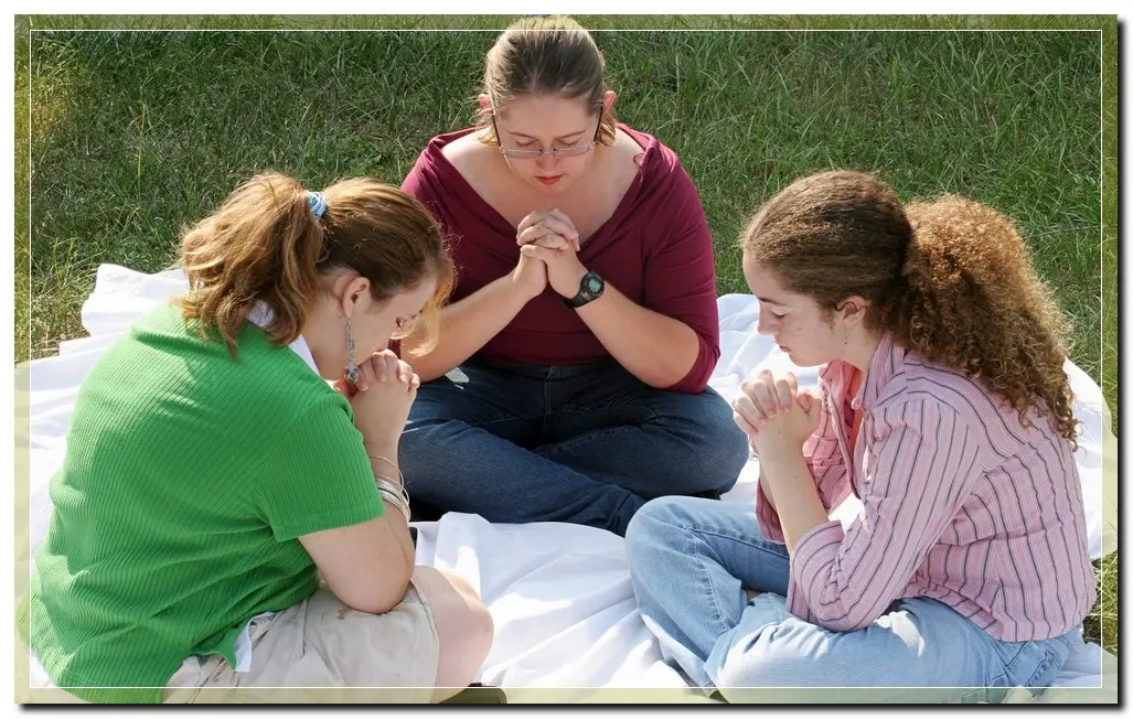 three women sitting outside, praying, at a christian drug rehab center