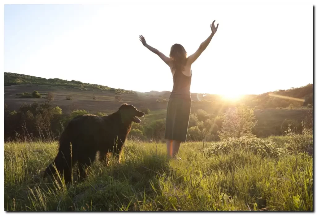 Woman in victory pose and dog in a field with sunset, sober living after going to treatment in a Private Drug Rehab Center in California
