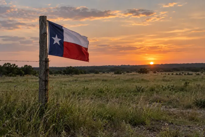 exas flag overlooking a rural field at sunset